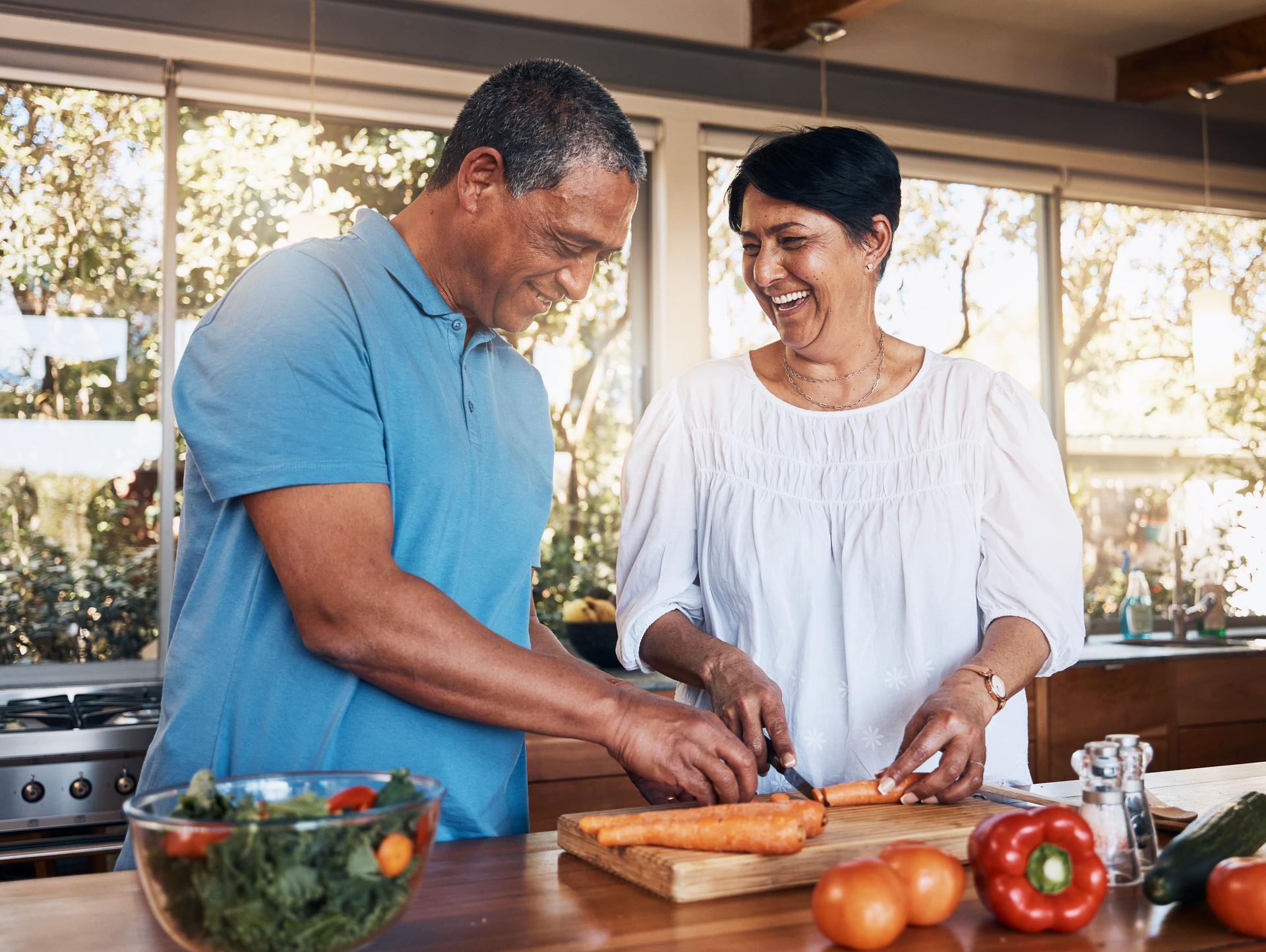 Cozinha madura, em casal e saudável na cozinha para picar legumes para dieta de salada, nutrição e almoço em casa. Homem feliz, mulher e ajudar a cortar ingredientes de cenoura para amor, cuidado e apoio juntos